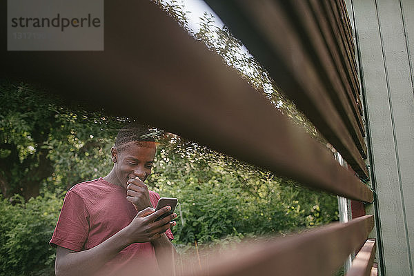 Lächelnder Junge mit Mobiltelefon durch den Zaun im Hinterhof gesehen