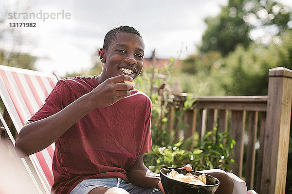 Porträt eines lächelnden Jungen  der einen Snack isst  während er auf der Veranda sitzt