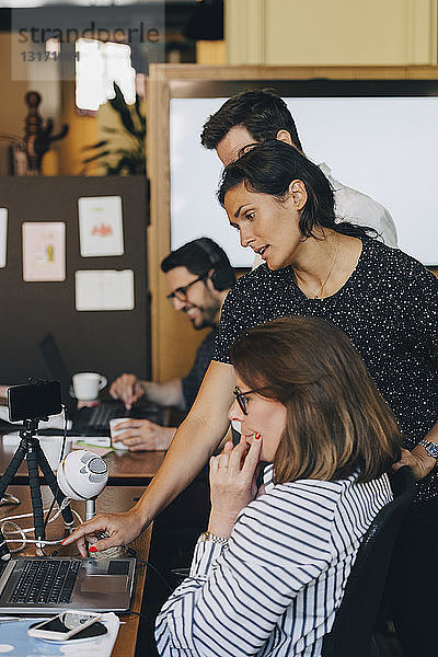 Mittlere erwachsene Geschäftsfrau diskutiert mit Team über Laptop im Büro