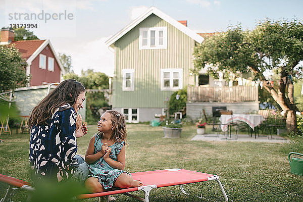 Lächelnde Mutter und Tochter unterhalten sich  während sie auf einem Liegestuhl im Hinterhof sitzen