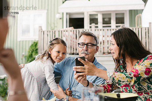 Mittelgroße erwachsene Frau zeigt der Familie ihr Handy  während sie im Hinterhof sitzt