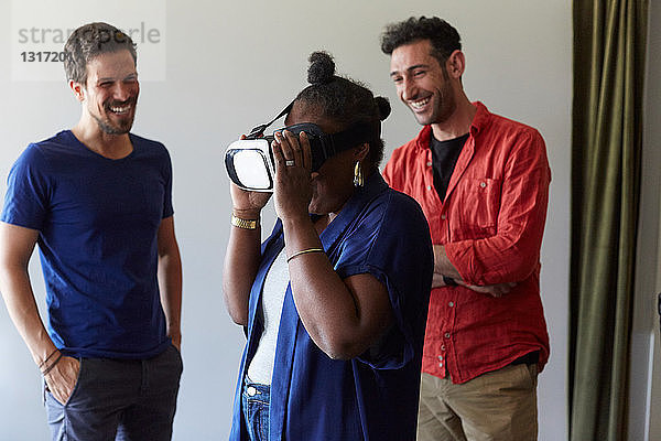 Geschäftsleute lächeln beim Anblick einer Kollegin  die einen Virtual-Reality-Simulator im Büro benutzt