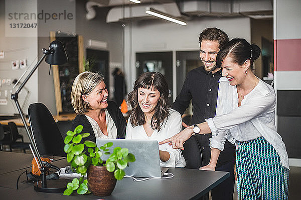 Kreative Geschäftsleute lächeln  während sie am Schreibtisch im Büro über den Laptop diskutieren