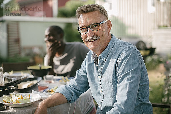 Porträt eines lächelnden älteren Mannes  der während einer Gartenparty am Tisch sitzt