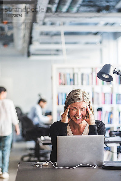 Geschäftsfrau lächelt  während sie im Büro auf den Laptop schaut