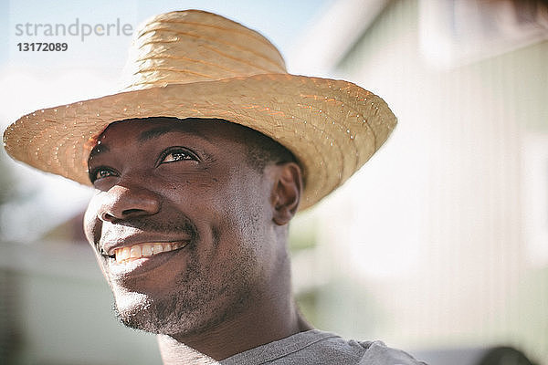 Lächelnder mittelgroßer Mann schaut weg  während er während der Gartenparty einen Strohhut trägt