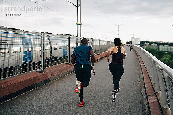 Rückansicht von männlichen und weiblichen Athleten  die auf einer Fußgängerbrücke in der Stadt laufen