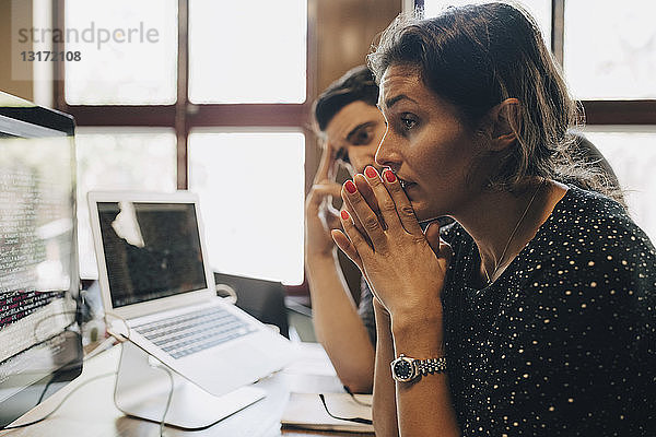 Angespannte  mittelgroße  erwachsene Geschäftsfrau mit verschränkten Händen  die im Büro auf den Computermonitor schaut