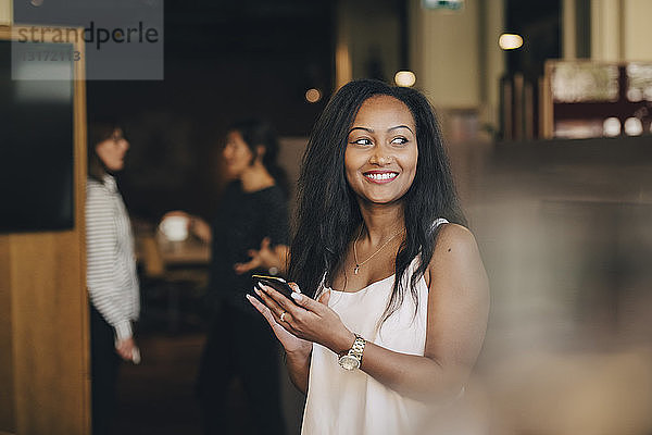 Lächelnde junge Geschäftsfrau benutzt Smartphone im Büro