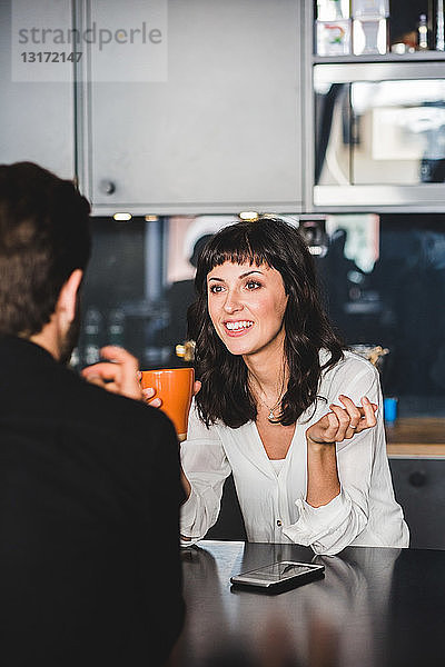 Geschäftsfrau lächelt beim Gespräch mit einem männlichen Kollegen am Tisch im Büro