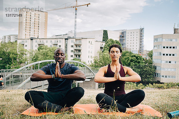Multi-ethnische Freunde praktizieren Yoga auf dem Feld gegen Gebäude in der Stadt