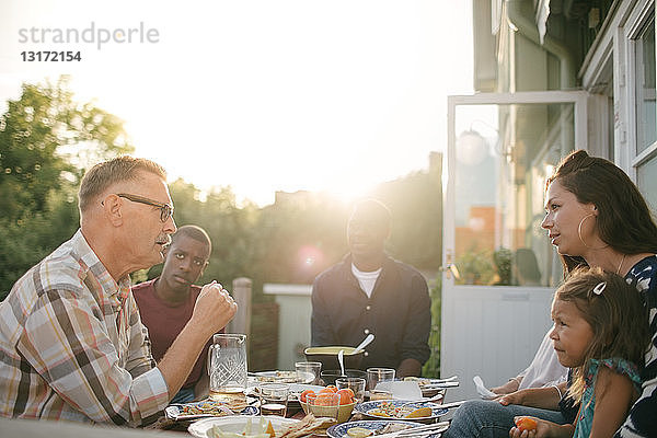 Mehrgenerationen-Familie isst bei Sonnenschein bei Tisch auf der Veranda zu Mittag