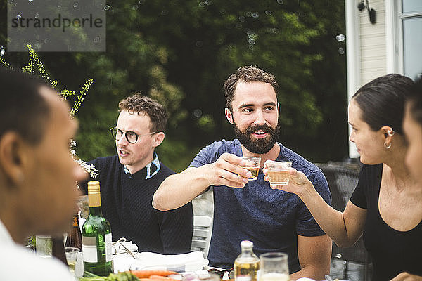 Mann und Frau stoßen bei einer Dinnerparty mit Freunden im Hinterhof auf Getränke an