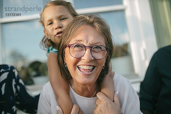 Glückliche ältere Frau  die ihre Enkelin auf der Veranda huckepack nimmt