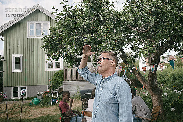 Älterer Mann schirmt Augen ab  wenn er während einer Gartenparty im Garten steht