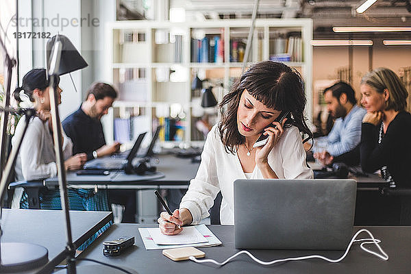 Geschäftsfrau  die während der Arbeit am Schreibtisch im Kreativbüro mit dem Handy telefoniert