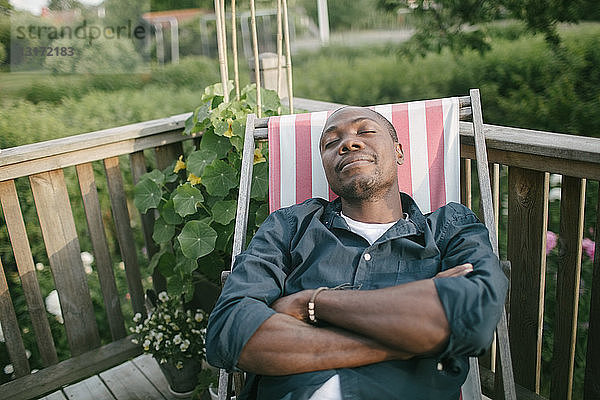 Mittelgroßer erwachsener Mann mit geschlossenen Augen  der sich auf einem Liegestuhl auf der Veranda entspannt