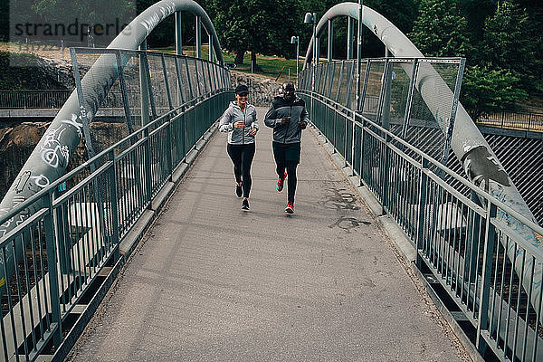 Männliche und weibliche Freunde in voller Länge joggen auf einer Fußgängerbrücke in der Stadt