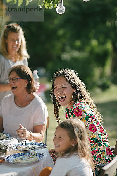 Glückliches Mädchen beim Mittagessen mit Mutter und Großmutter am Tisch während der Gartenparty