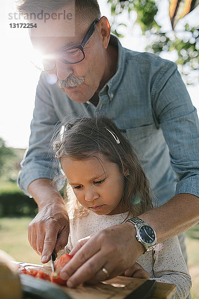 Großvater lehrt Enkelin  Tomaten bei Tisch im Hinterhof zu schneiden