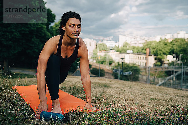 Junge Frau mit geschlossenen Augen praktiziert Yoga auf einem Feld in der Stadt