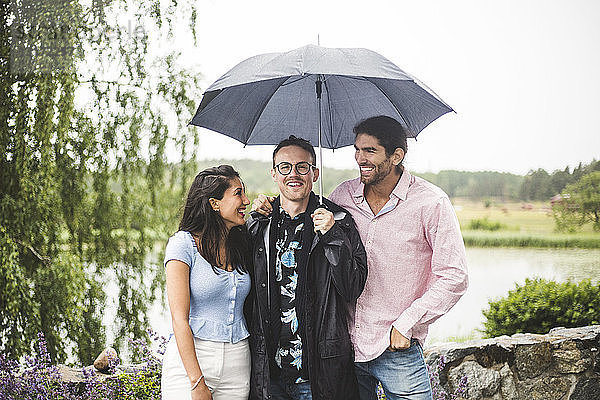 Glückliche Freunde stehen während des Wochenendausflugs unter dem Regenschirm