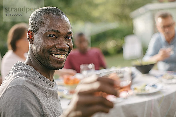 Porträt eines lächelnden mittelgroßen Mannes  der während einer Gartenparty ein Getränk in der Hand hält