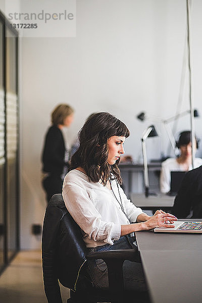 Unternehmerin benutzt Laptop  während sie am Schreibtisch im Kreativbüro sitzt