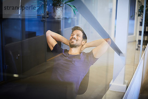 Kreativer Geschäftsmann entspannt sich auf einem Stuhl mit Blick durch Glas im Büro