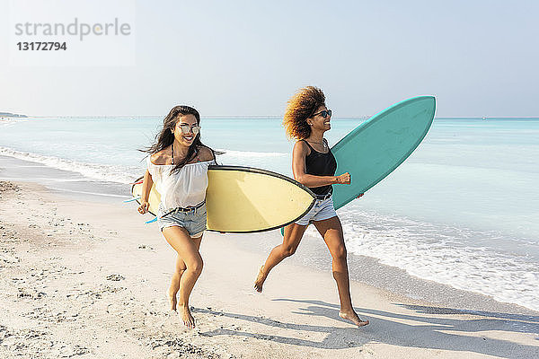 Freundinnen laufen am Strand und tragen Surfbretter