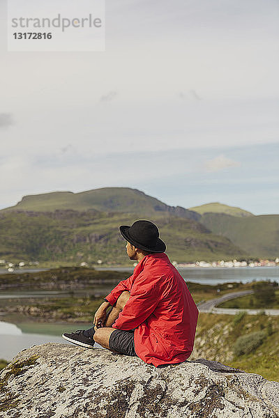 Auf einem Felsen sitzender junger Mann auf der Insel Vesteralen  Lappland  Norwegen