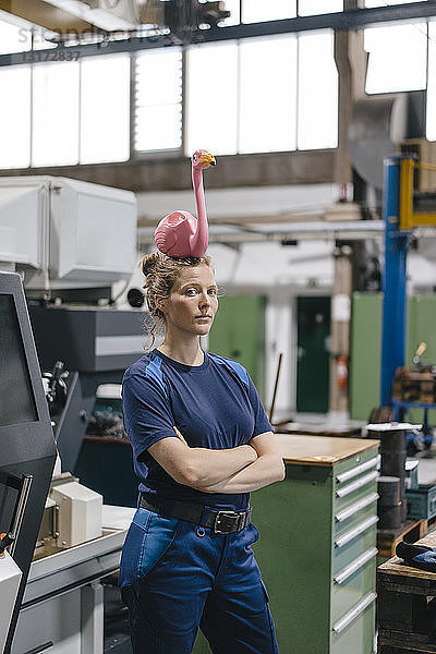 Junge Frau arbeitet als Facharbeiterin in einem High-Tech-Unternehmen und balanciert einen rosa Flamingo auf ihrem Kopf