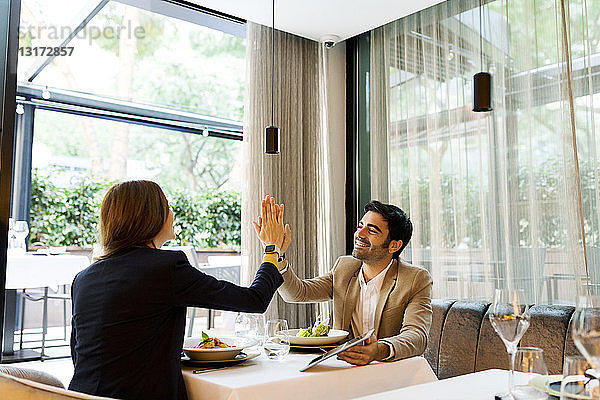 Glücklicher Mann und Frau mit einer Tablette in einem Restaurant High Fiving