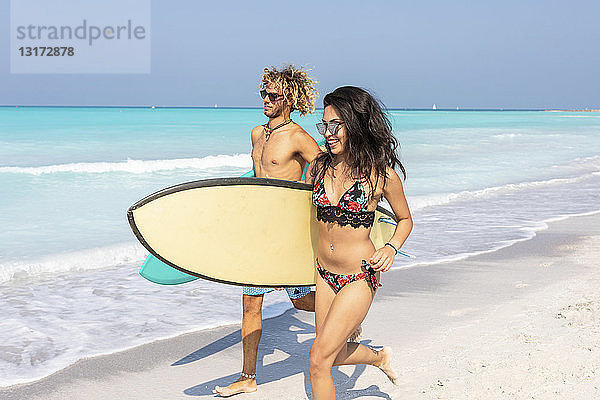 Paar  das am Strand läuft und Surfbretter trägt