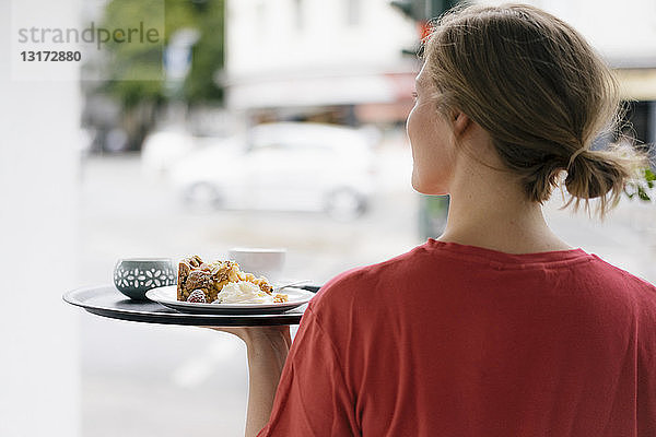 Rückansicht einer jungen Frau  die in einem Cafe Kaffee und Kuchen serviert