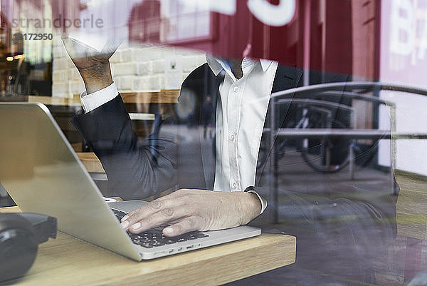 Leitender Geschäftsmann hinter einer Fensterscheibe in einem Café  der am Laptop arbeitet