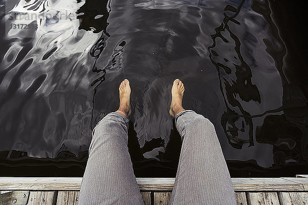 Mann sitzt auf einem Steg an einem See und baumelt mit den Füßen im Wasser