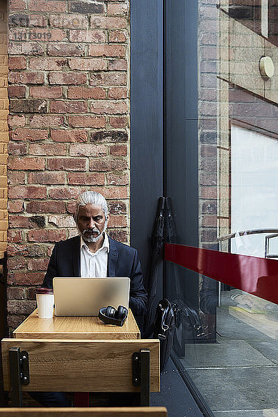 Leitender Geschäftsmann arbeitet am Laptop in einem Café