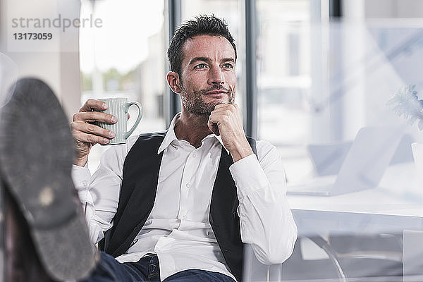 Geschäftsmann sitzt im Büro  trinkt Kaffee  mit erhobenen Füßen