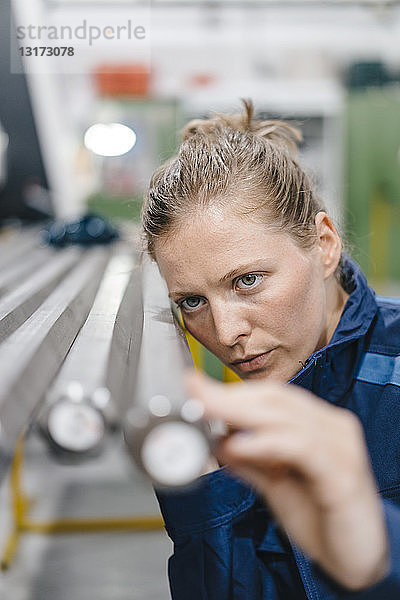 Junge Frau  die als Facharbeiterin in einem High-Tech-Unternehmen arbeitet und Stahlstäbe kontrolliert