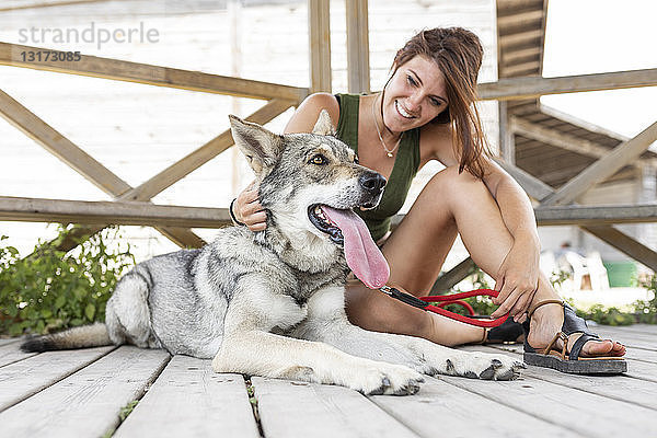 Lächelnde junge Frau streichelt ihren Hund auf einer Terrasse