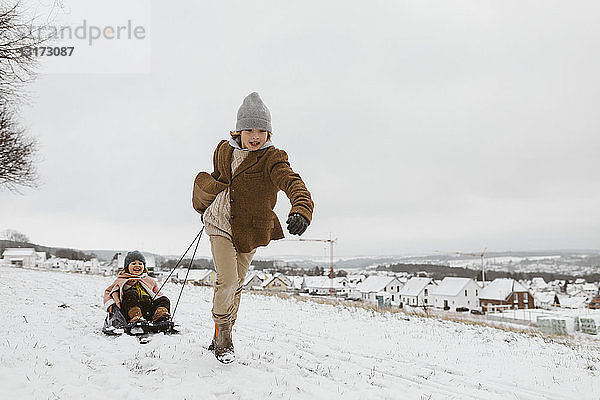 Junge zieht Schlitten mit kleiner Schwester im Schnee