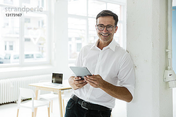 Porträt eines glücklichen Geschäftsmannes mit Tablett im hellen Büro