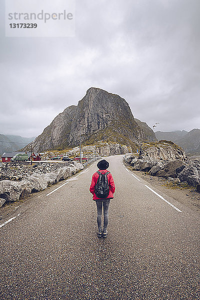 Norwegen  Lofoten  Hamnoy  Rückenansicht eines Mannes mit Rucksack  der auf einer leeren Straße steht