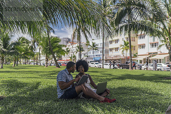 USA  Florida  Miami Beach  junges Paar mit Tablet und Laptop auf einem Rasen in einem Park