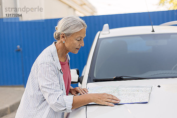 Ältere Frau betrachtet Straßenkarte auf der Motorhaube ihres Autos
