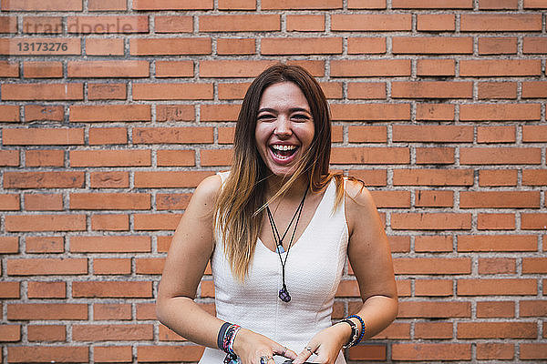 Porträt einer lachenden jungen Frau  die vor einer Ziegelmauer steht