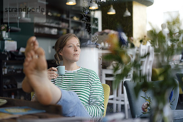 Junge Frau mit erhobenen Füßen  die in einem Café eine Espressotasse hält