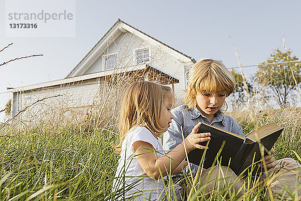 Bruder und seine kleine Schwester sitzen auf einer Wiese und lesen ein Buch