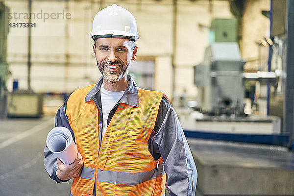 Porträt eines lächelnden Mannes mit Blaupausen in der Fabrik